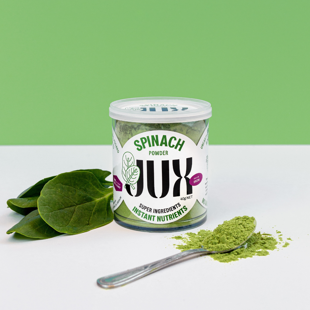 JUX Freeze-dried Spinach powder in pot and on a teaspoon next to a fresh spinach leaf