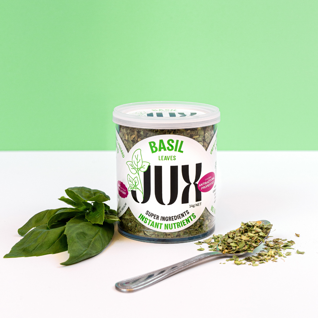 Freeze-dried Basil leaves in a clear jar branded with JUX next to fresh basil 
