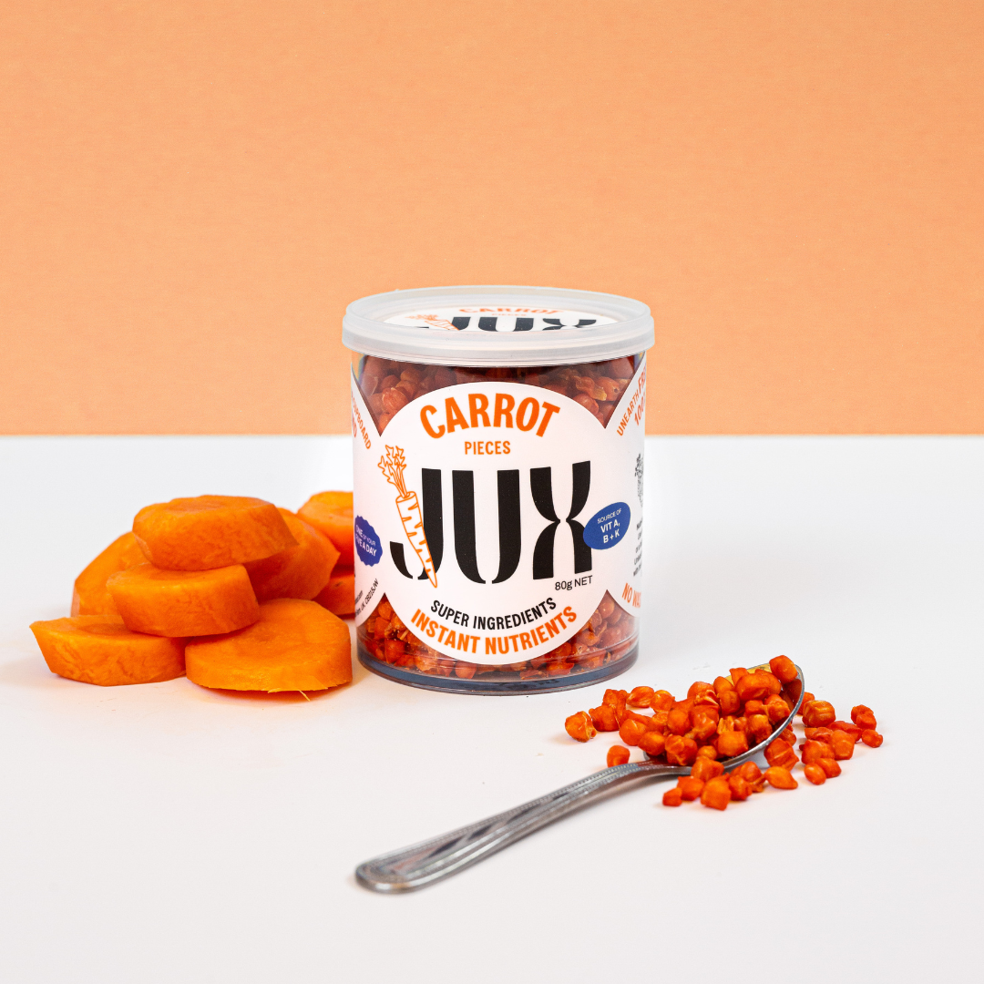 Jar of JUX Freeze-dried Carrot pieces beside a teaspoon and fresh carrots